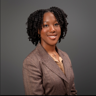 Denese Kellier stands facing the camera from a semi-right angle. She wears a beige suit and beige blouse.